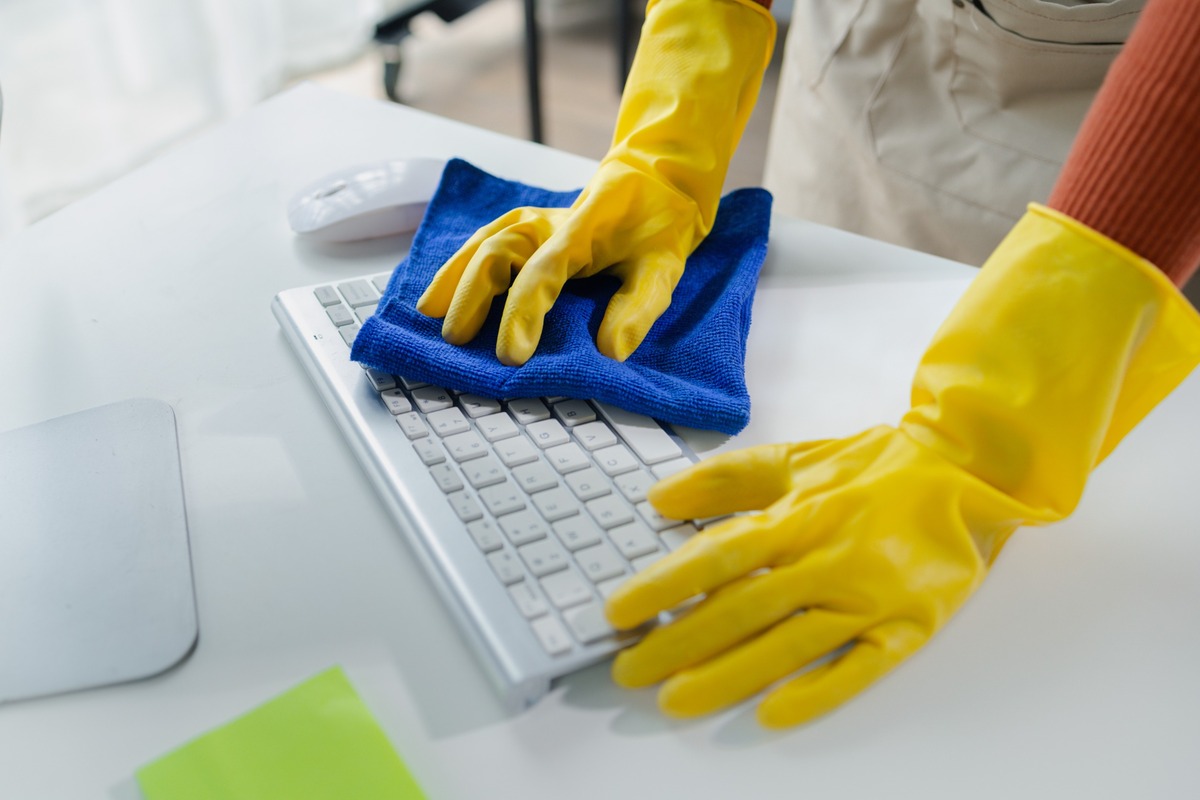 manos de personal de limpeiza con guantes amarillos pasan bayeta por teclado en oficina